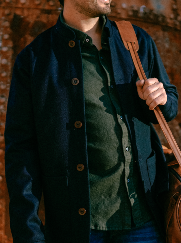 Front of the Tambo Wool Jacket in Navy, open over an olive shirt, with a brown leather shoulder bag