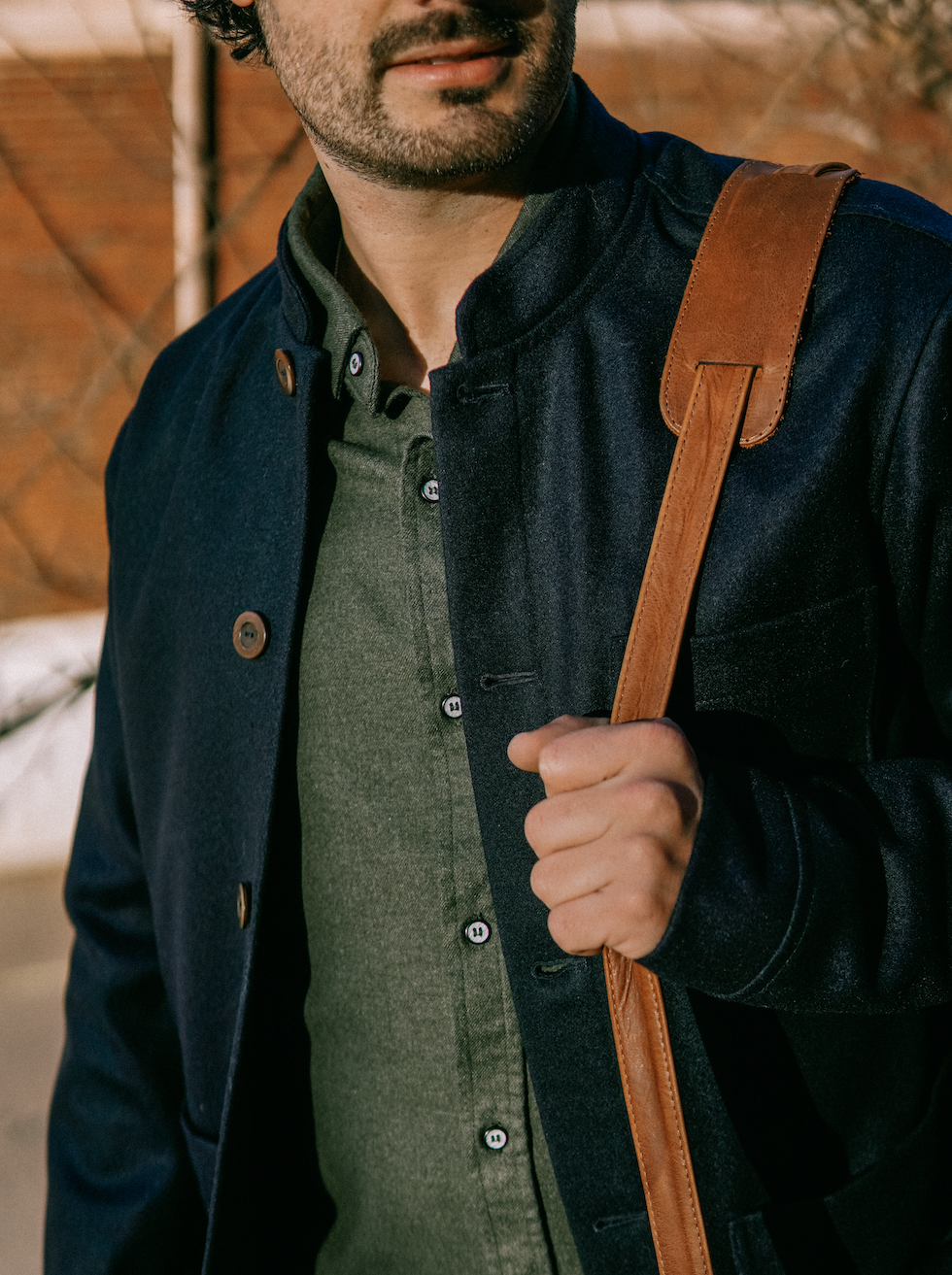 Tambo Wool Jacket in Navy over an olive shirt, with a leather bag strap on the shoulder