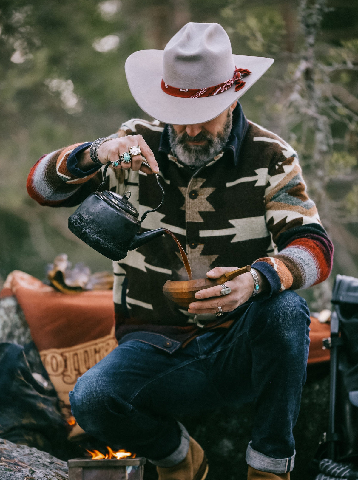 Man in a white hat kneeling by a motorcycle in the Peguche Jacket, dark brown with cream Andean pattern